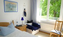 Schlafzimmer mit großem Fenster und Blick auf große Bäume, Aufbettung für eine weitere Person möglich